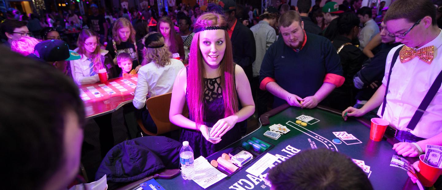 Student Program Board web banner image, a crowded room depicting a casino night, featuring a girl dressed as a flapper dealing cards to a table