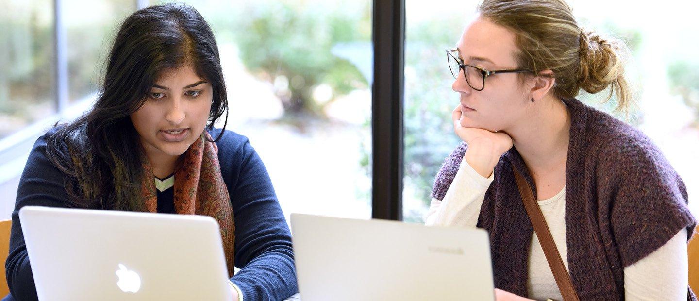 two women seated behind open laptops