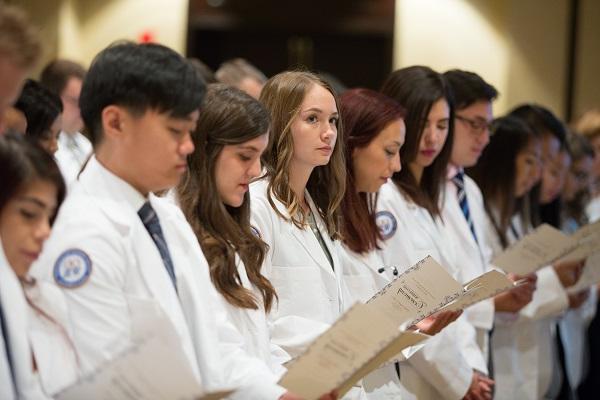 学生 stand, holding programs, at the white coat ceremony.