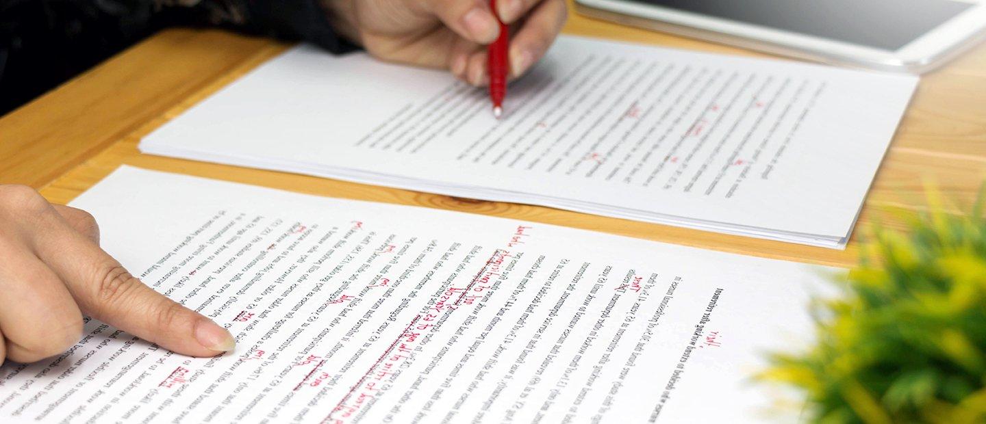 A person proof-reading a document and marking corrections in red pen.